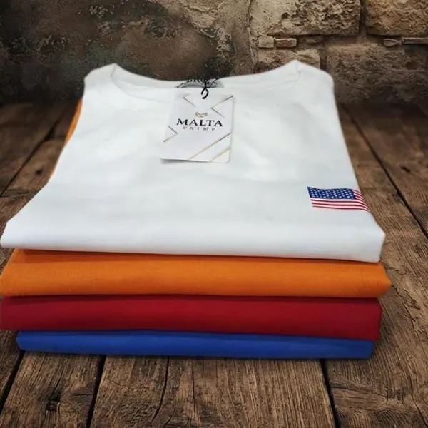 Camisetas Malta Roots dobradas sobre mesa de madeira rústica
