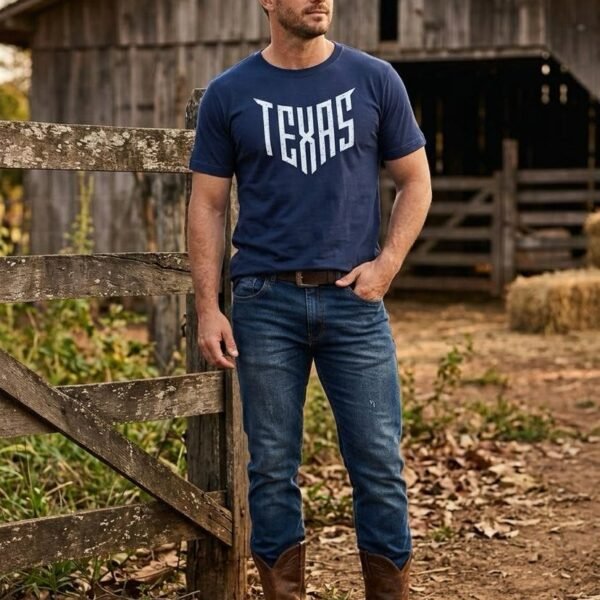 Homem de camiseta azul-marinho Texas Shield encostado na porteira de um curral